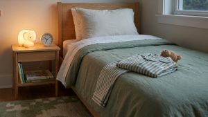 Young child's bed with pajamas, books, a clock, and a soft night light for a back to school sleep reset.
